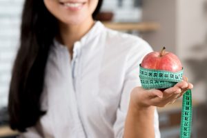 close-up-woman-s-hand-holding-red-apple-with-green-measurement-tape_23-2148076038